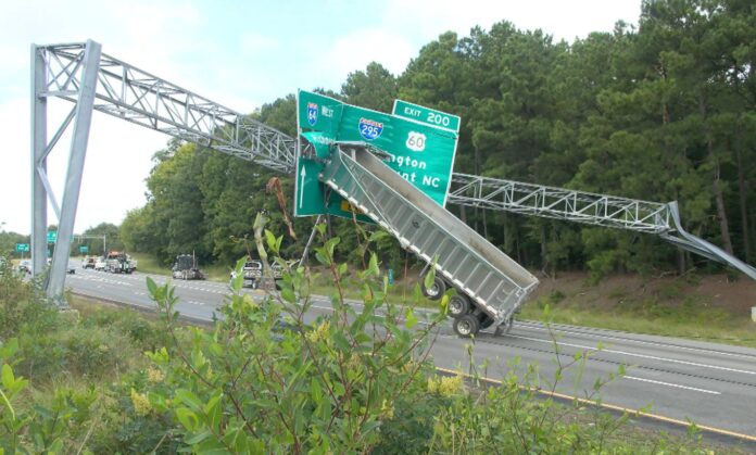 PHOTO: Trailer truck hanging on I-64 West Richmond – Washington Mount NC road signboard as driver, Richard D. Houston, Jr, didn’t lower the tipper before accident